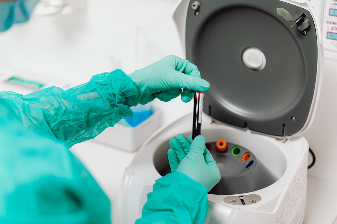 Lab technician operates a centrifuge machine, handling tubes with gloves.