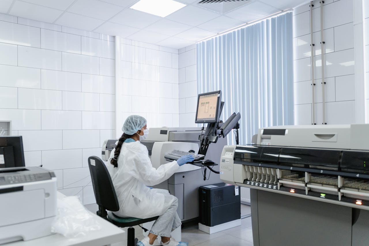 A laboratory technician wearing protective gear operates medical equipment in a sterile lab environment.